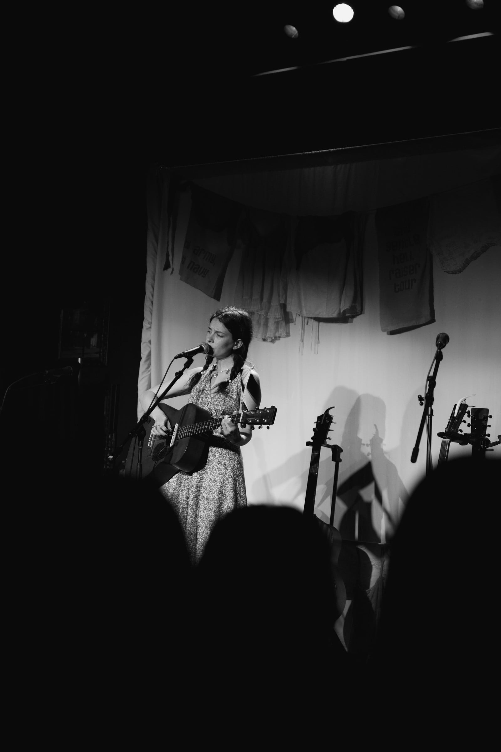 A black-and-white view of an acoustic performer on stage above the audience silhouettes.