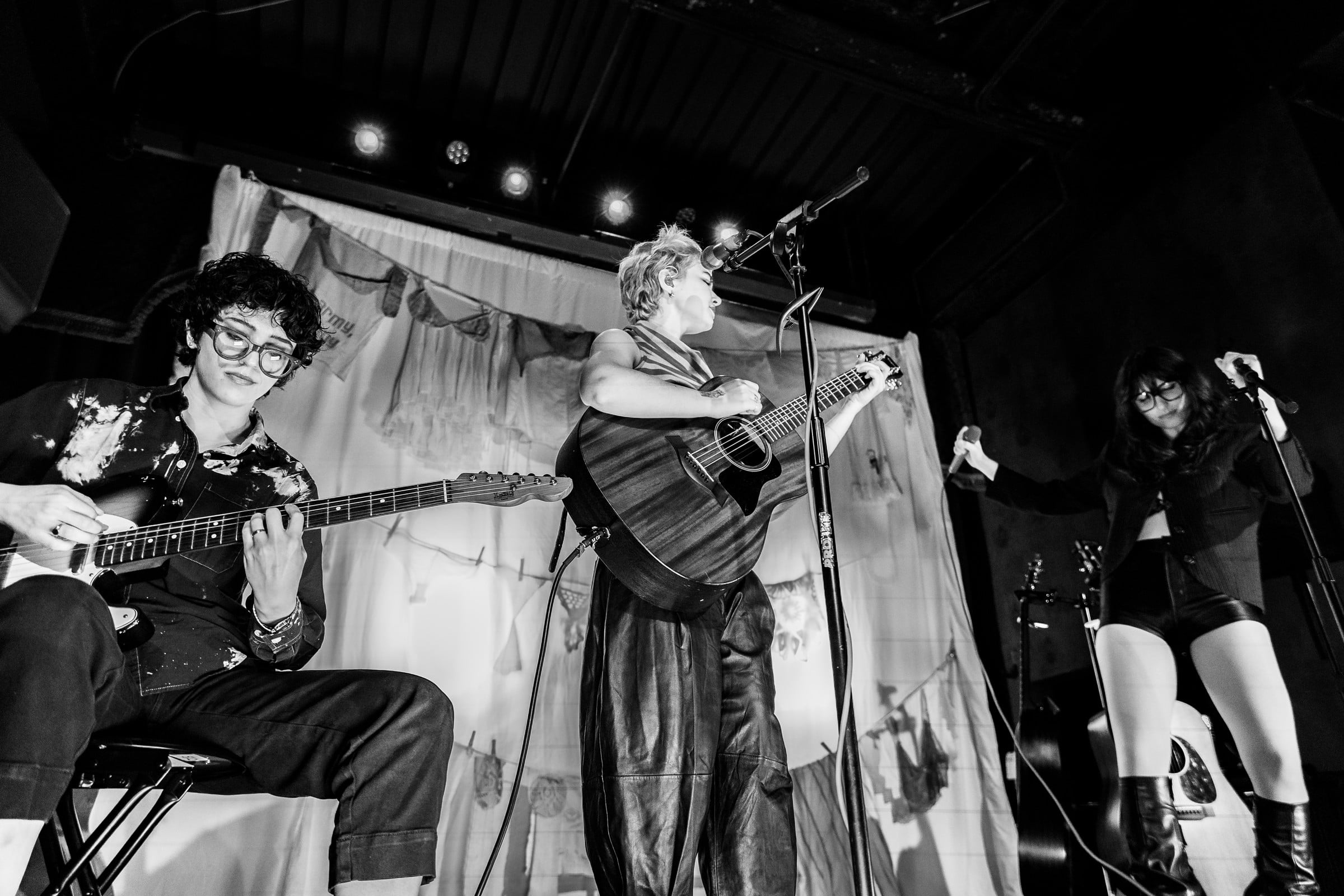 Musicians performing together on a small stage, photographed in black and white.
