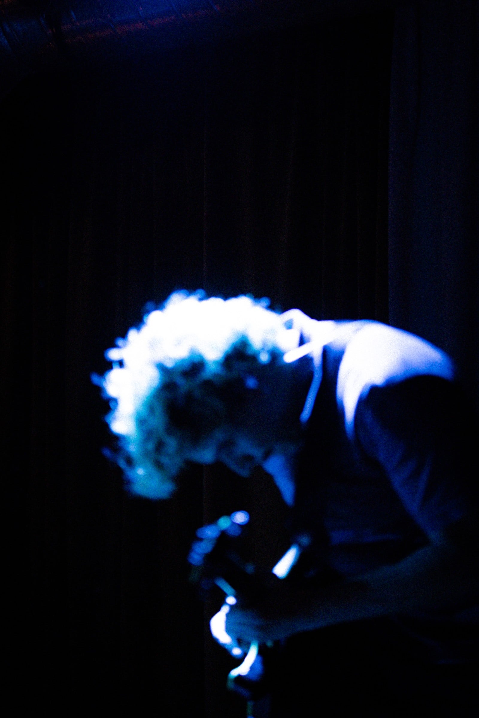 A deliberately soft, blue-lit view of a guitarist leaning into a performance.