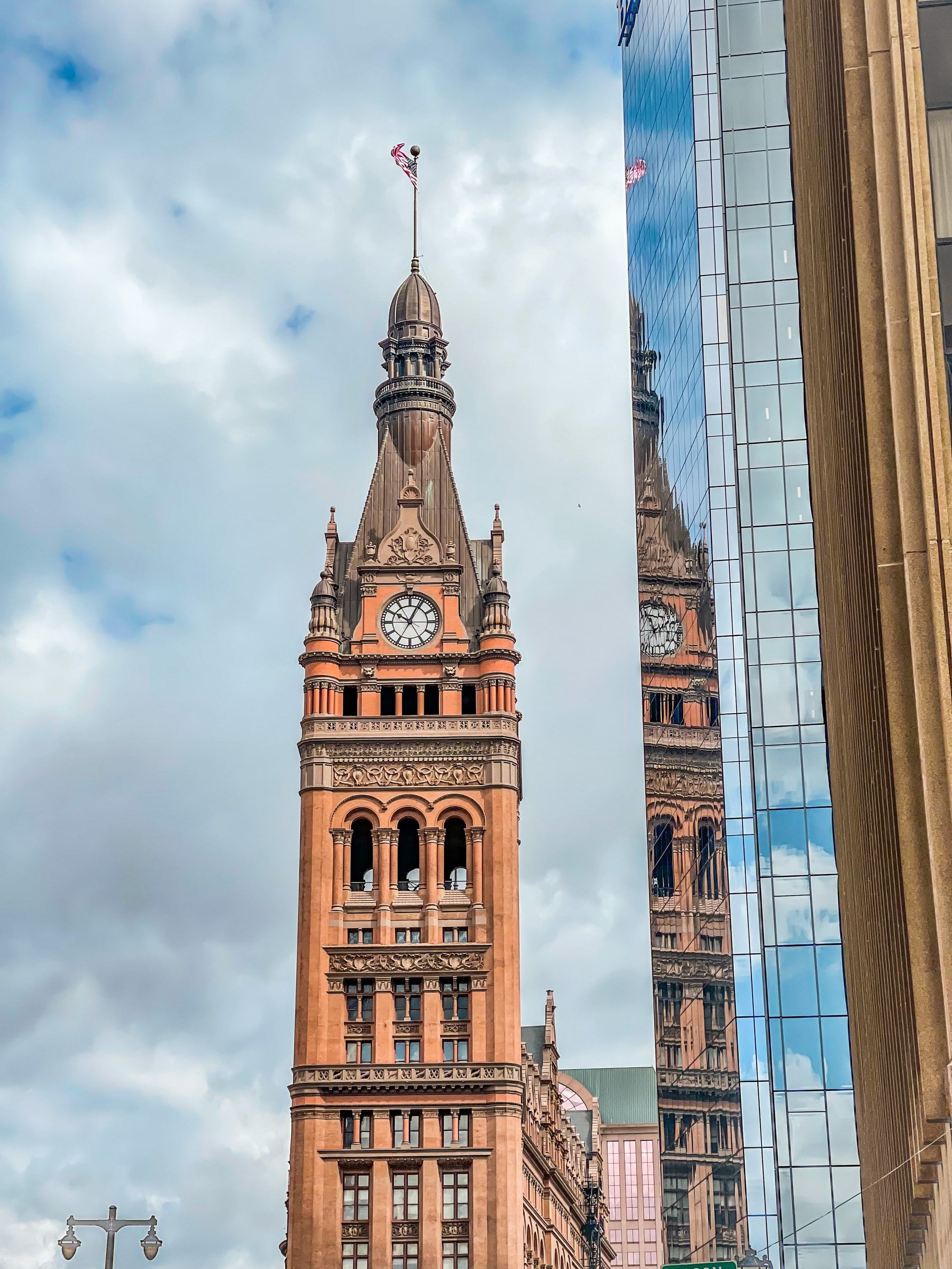 A brick clock tower beside a glass building reflecting its facade.