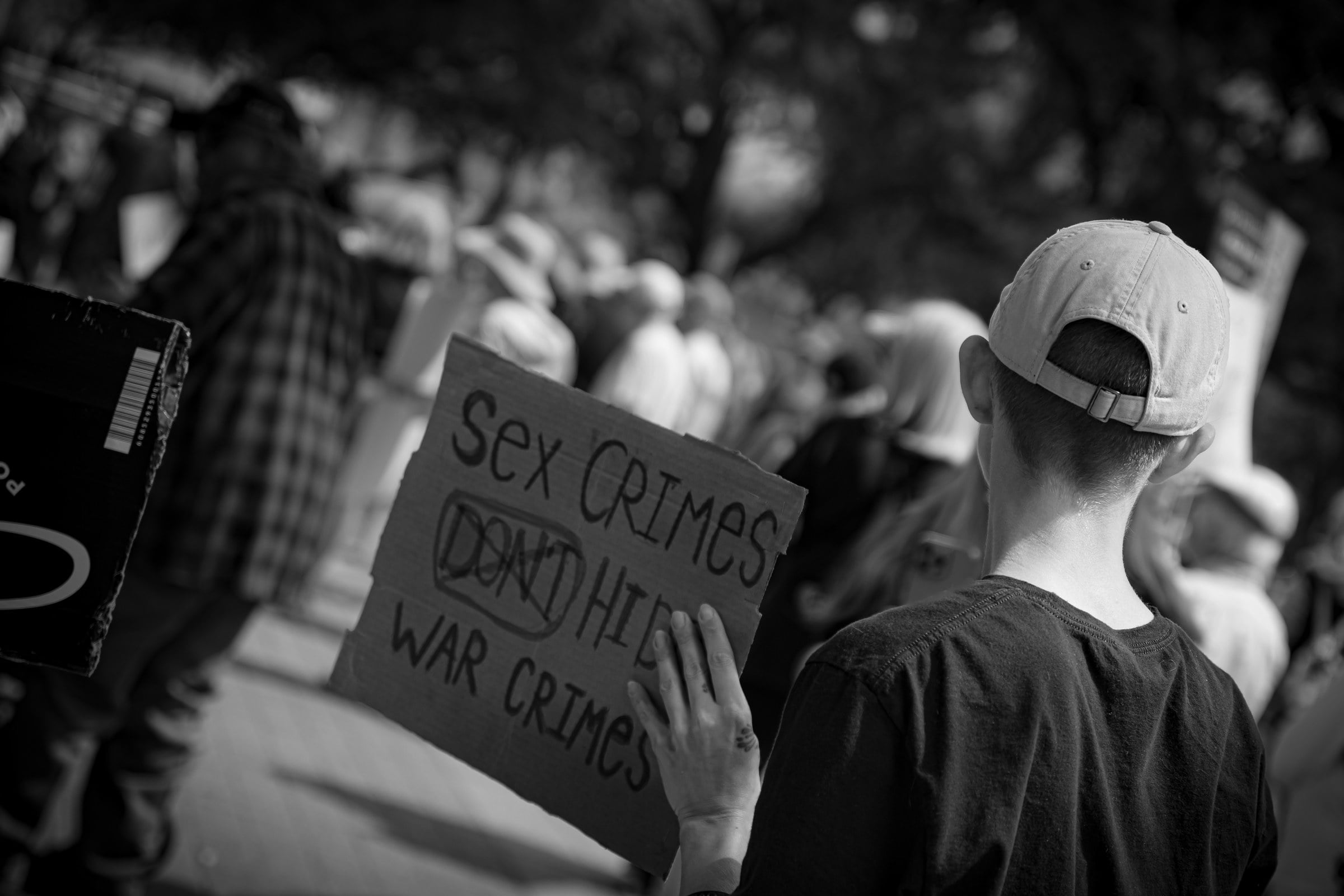 A black-and-white view of people in a crowd, including someone holding a handwritten sign.