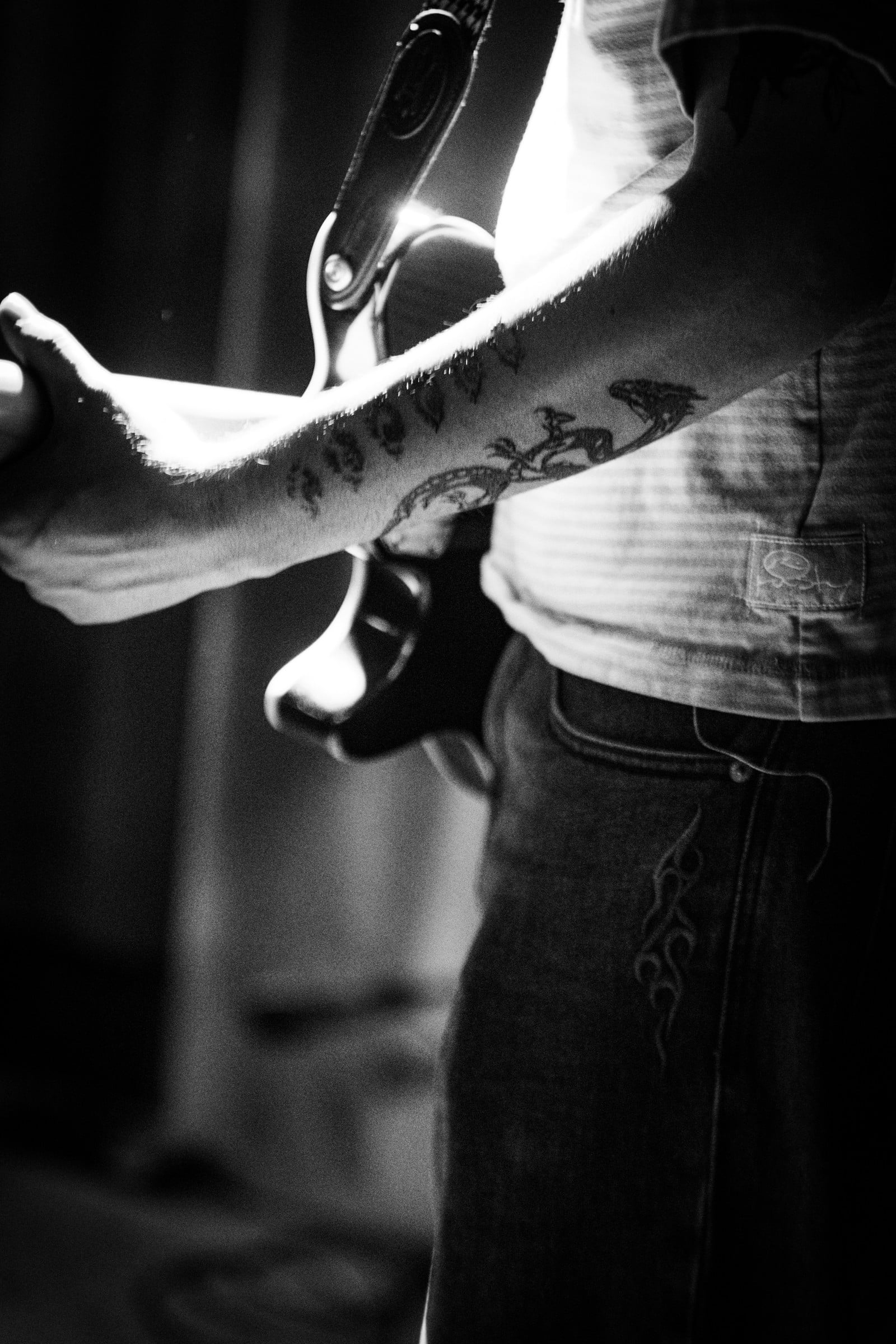 A black-and-white detail of a tattooed forearm and an electric guitar.