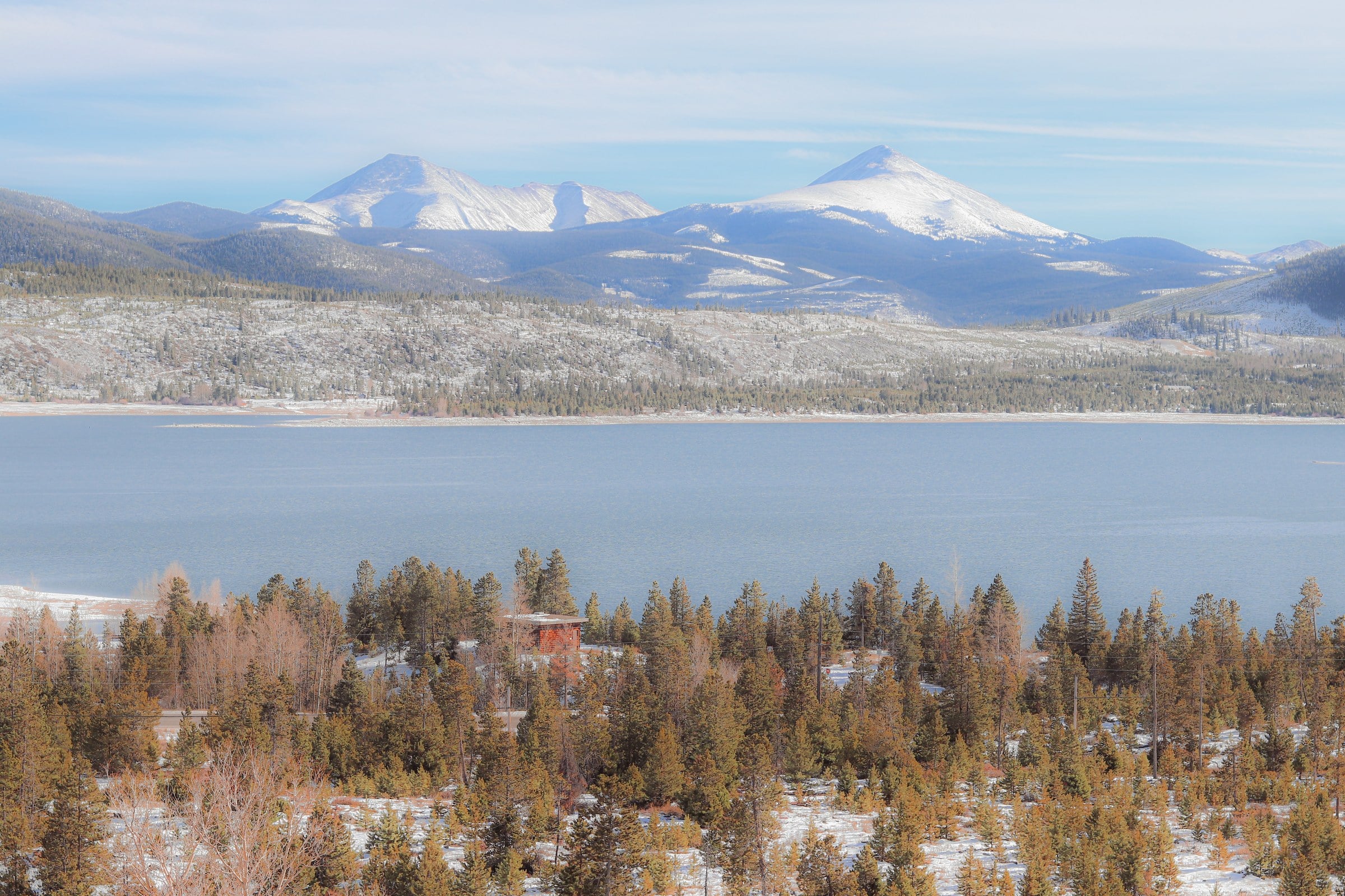 A lake surrounded by snowy forest and distant mountain peaks.
