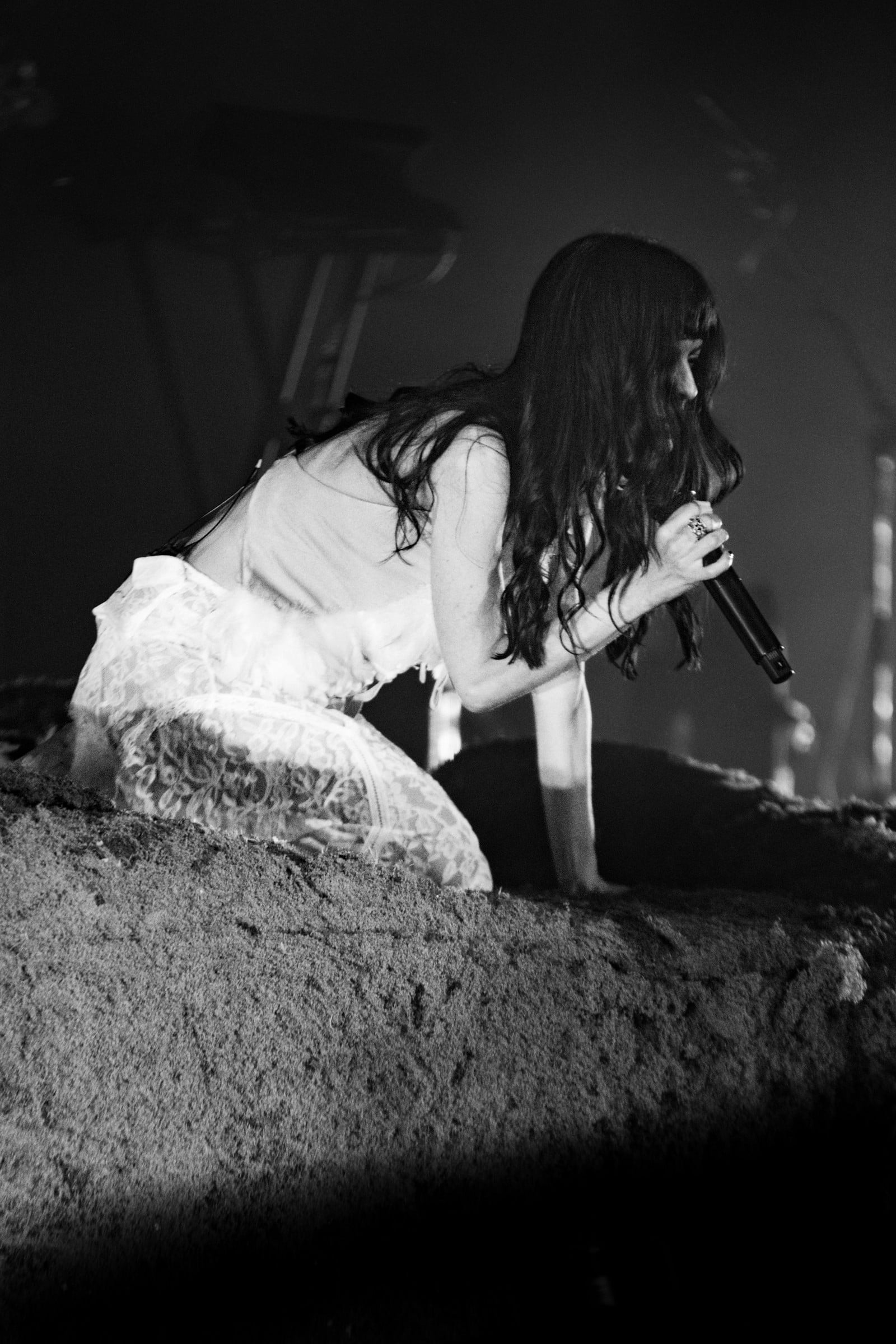 A black-and-white view of a vocalist leaning low across a textured stage set.