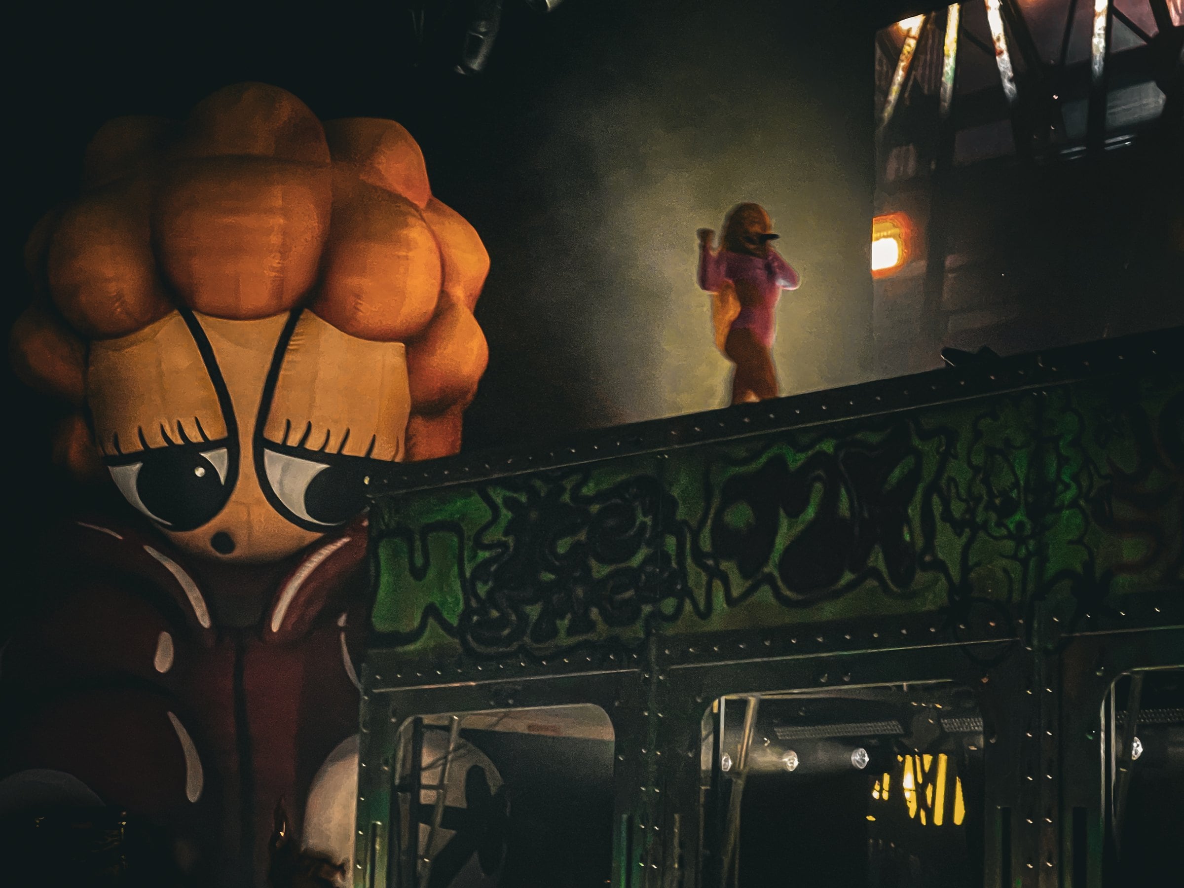 A singer performing above a theatrical stage set beside an oversized orange character face.