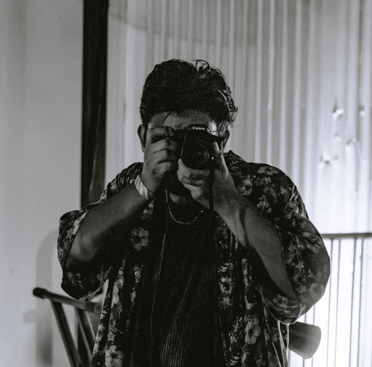 Jeremy Jakob holding a camera to his face in a black-and-white mirror portrait.